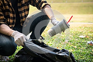 Volunteer man in gloves sitting to picking up coffee cup into plastic black bag for cleaning the park