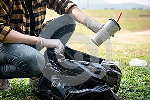 Volunteer man in gloves sitting to picking up coffee cup into plastic black bag for cleaning the park