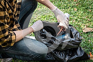 Volunteer man in gloves sitting to picking up coffee cup into plastic black bag for cleaning the park