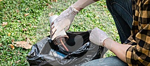 Volunteer man in gloves sitting to picking up coffee cup into plastic black bag for cleaning the park