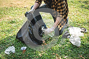 Volunteer man in gloves sitting to picking up plastic bottle and plastic waste into plastic black bag