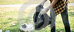Volunteer man in gloves to picking up plastic bottle into plastic black bag for cleaning the park