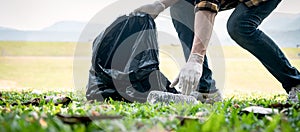 Volunteer man in gloves walking and stooping to collect plastic bottles into plastic black bag for cleaning