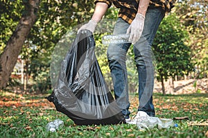 Volunteer man in gloves walking to carrying plastic black bag and collecting plastic bottles into bag