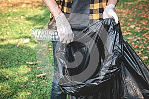 Volunteer man in gloves walking to carrying plastic black bag and collecting plastic bottles into bag