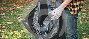 Volunteer man in gloves walking to carrying plastic black bag and collecting plastic bottles into bag