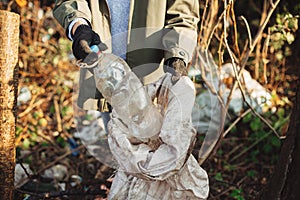 Volunteer picking up dirty plastic bottles in park. Woman hand in glove picking up trash, collecting garbage in bag. Cleaning up