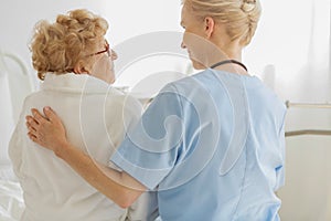 Volunteer sitting on a hospice bed next to an senior resident and strokes her back