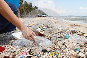 Volunteer tourist hand is clean up garbage and plastic debris on dirty beach by collecting them into big blue bag