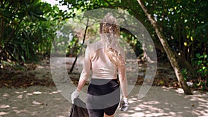 Volunteer with trash bag collects rubbish at tropical beach, combats pollution. Eco-friendly female removes litter