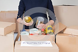 Volunteer woman collecting food into donations box. Cardbox full of grocery products. Donation, charity, food bank, help