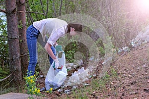 Volunteer woman picking trash on forest near lake in park, collecting garbage.