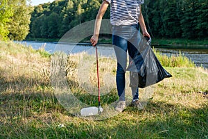 Volunteer woman picking up plastic garbage on coast of the river. Cleaning environment concept