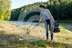 Volunteer woman picking up plastic garbage on coast of the river. Cleaning environment concept