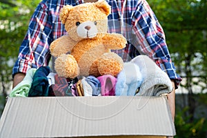 Volunteer woman provide clothing donation box with used clothes and doll to support help for refugee, homeless or poor people in