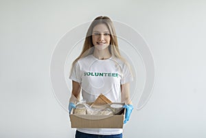 Volunteer work. Happy woman in volunteer t-shirt and medical gloves, holding food donations box and smiling at camera