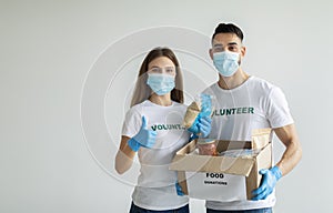 Volunteer work. Young happy volunteers in medical masks holding food donations box, woman showing thumb up, copy space