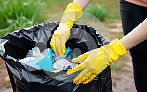Volunteer in yellow gloves collects garbage in nature