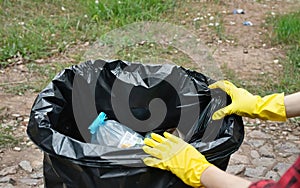 volunteer in yellow gloves and garbage collected in nature in a black bag