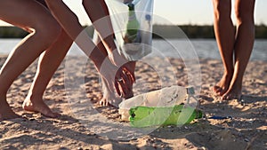 Volunteer young women cleaning up the dirty beach from plastic carrying bags to collect trash on sunny day at a lake