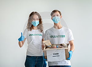Volunteering concept. Young volunteers in medical masks holding food donations box and woman showing thumb up