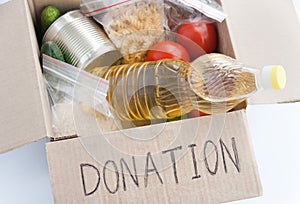 Volunteering donation concept. Food for donation in a cardboard box. Oil, canned foods, tomatoes, cucumbers and cereals. Close up