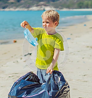 Volunteers beach sand lazur sea. Boy pick up garbage into black bag. Son refuse to wear blue face mask because tired photo