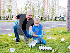 Volunteers dad and son clean up plastic and paper trash from the green lawn near the apartment building with trash tongs