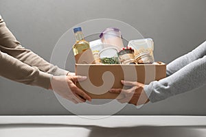 Volunteers with donation box with foodstuffs on grey background