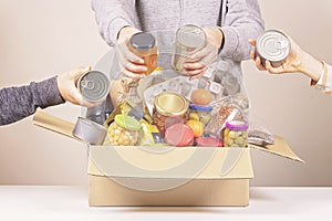 Volunteers hands collecting grocery products to food donations box for poor family, homeless people