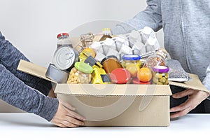 Volunteers hands holding food donations box with grocery products on white desk