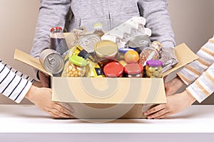 Volunteers hands holding food donations box with grocery products on white desk