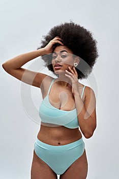 Voluptuous young mixed race female model with afro hair wearing blue underwear posing for camera, standing isolated over