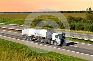 Volvo heavy fuel tanker truck by `GAZPROM` driving on highway on sunset background. Out of focus, possible granularity, motion