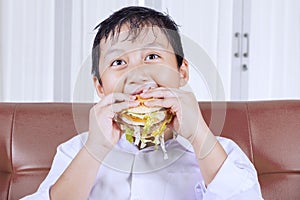 Voracious little boy eating a burger at home