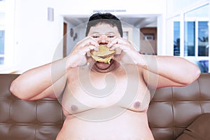 Voracious obese man eating a hamburger at home