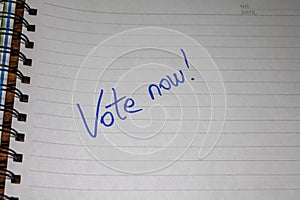 Vote now, handwriting  text on paper, political message. Political text on office agenda. Concept of democracy, voting, politics.