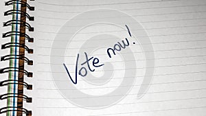 Vote now, handwriting  text on paper, political message. Political text on office agenda. Concept of democracy, voting, politics.