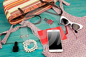 Voyage concept - set of woman stuff with dress, smart phone, bag, notepad, accessory and nail polishes on wooden desk