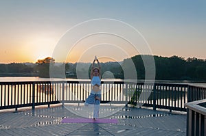 Vrikshasana pose. Young woman is doing yoga on the sunrise