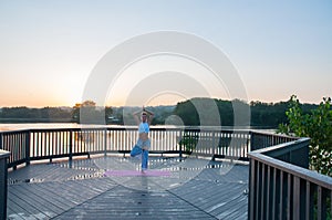 Vrikshasana pose. Young woman is doing yoga on the sunrise