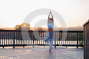 Vrikshasana pose. Young woman is doing yoga on the sunrise