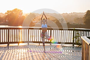 Vrikshasana pose. Young woman is doing yoga on the sunrise