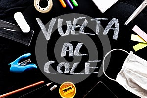 Vuelta al cole text in spanish, meaning back to school, with covid face mask on desk in classroom and stationery equipment. photo
