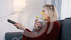 Vulnerable old woman in quarantine using oxygen inhaler and changing chanels on tv