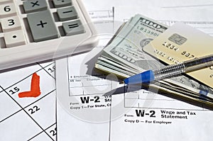 W-2 Wage and Tax statement blank with credit card on dollar bills, calculator and pen on calendar page with marked 15th April