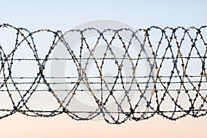 W rapped barbed wire fence with spikes and sky in the background. Rusted chain link fence guarding high security facility like