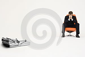 Wad of cash on mouse trap with worried businessman sitting on chair representing financial difficulties