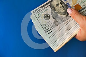 A wad of hundred-dollar bills held in his hand against a bright blue background. The concept of cash, give money on credit, pay in