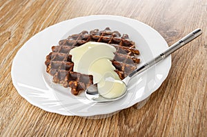 Wafer in chocolate poured condensed milk, spoon in plate on wooden table